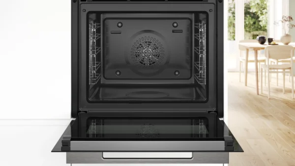 Open front view of a modern black oven with racks on both sides and a circular fan in the back set in a bright kitchen with a wooden dining table in the background Globalmtc