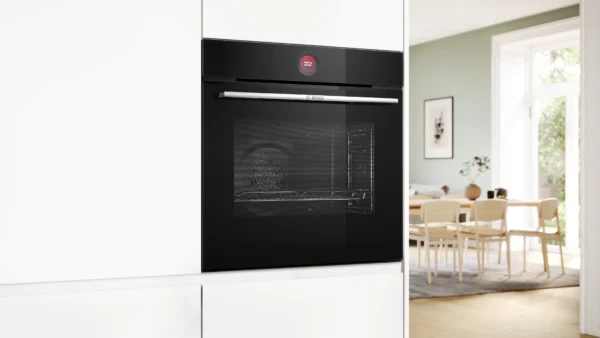 Built in black oven with a silver handle set in white cabinets a dining room is visible through an open doorway in the background Globalmtc