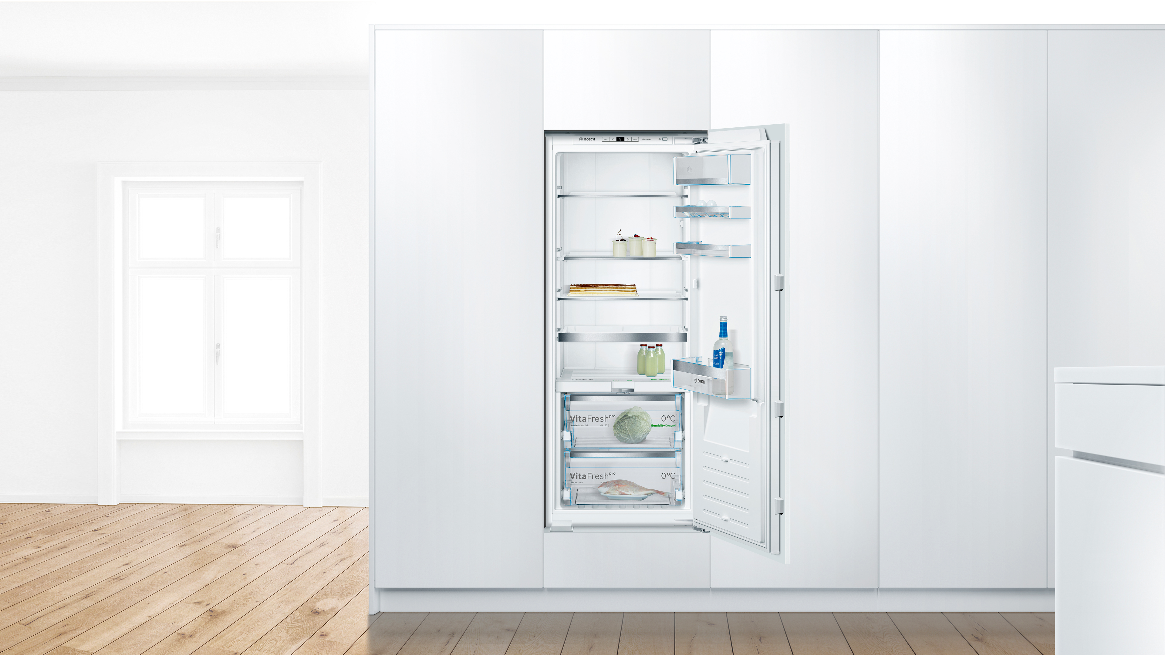 Open built in refrigerator in a bright white kitchen showing shelves with milk bottles jars and bread inside Globalmtc
