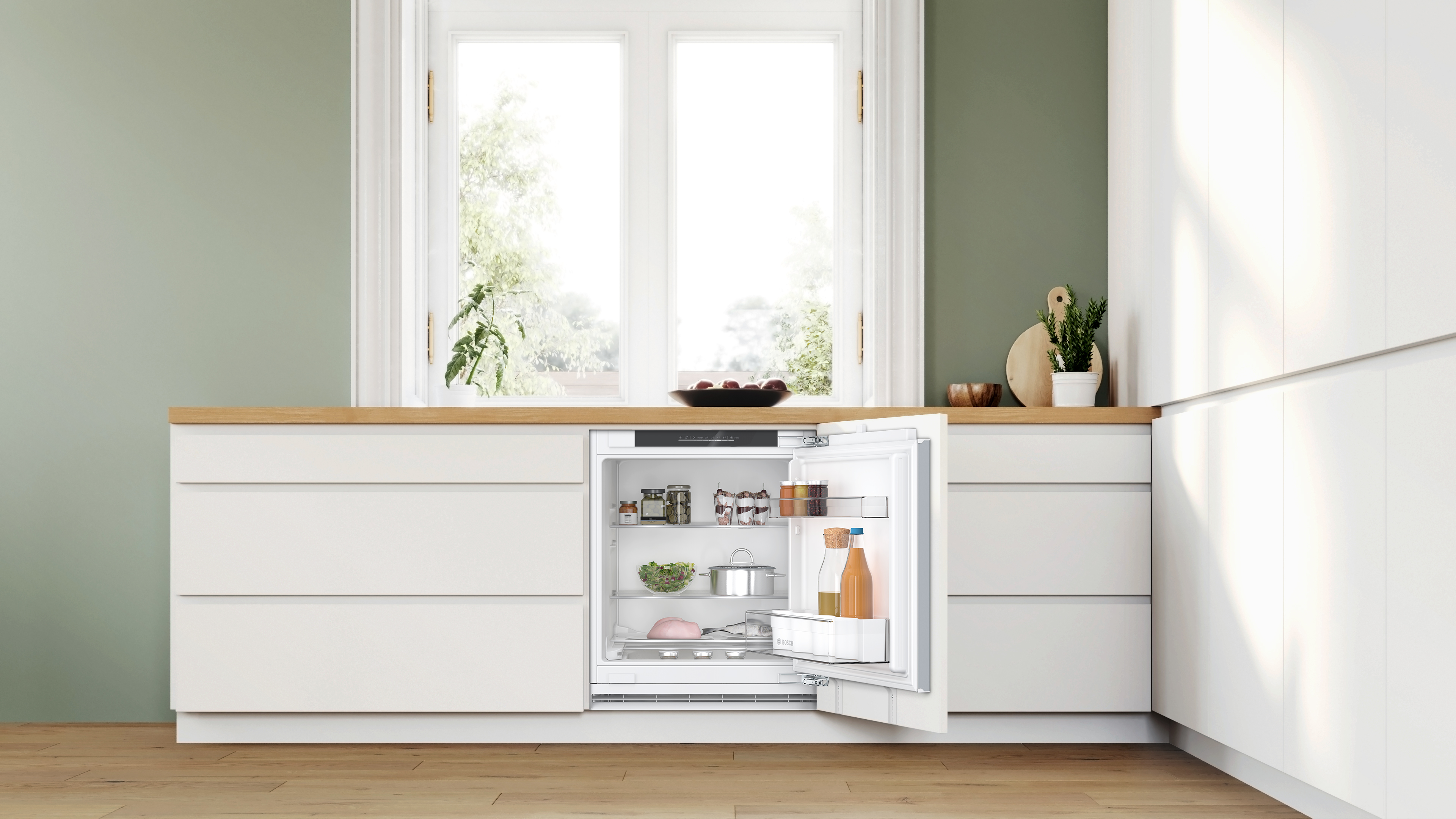 Modern white kitchen with a built in open fridge revealing jars bottles and pantry items on glass shelves against a green wall and wooden counter Globalmtc